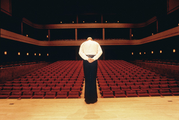 Man Bowing on Stage in Empty Concert Hall